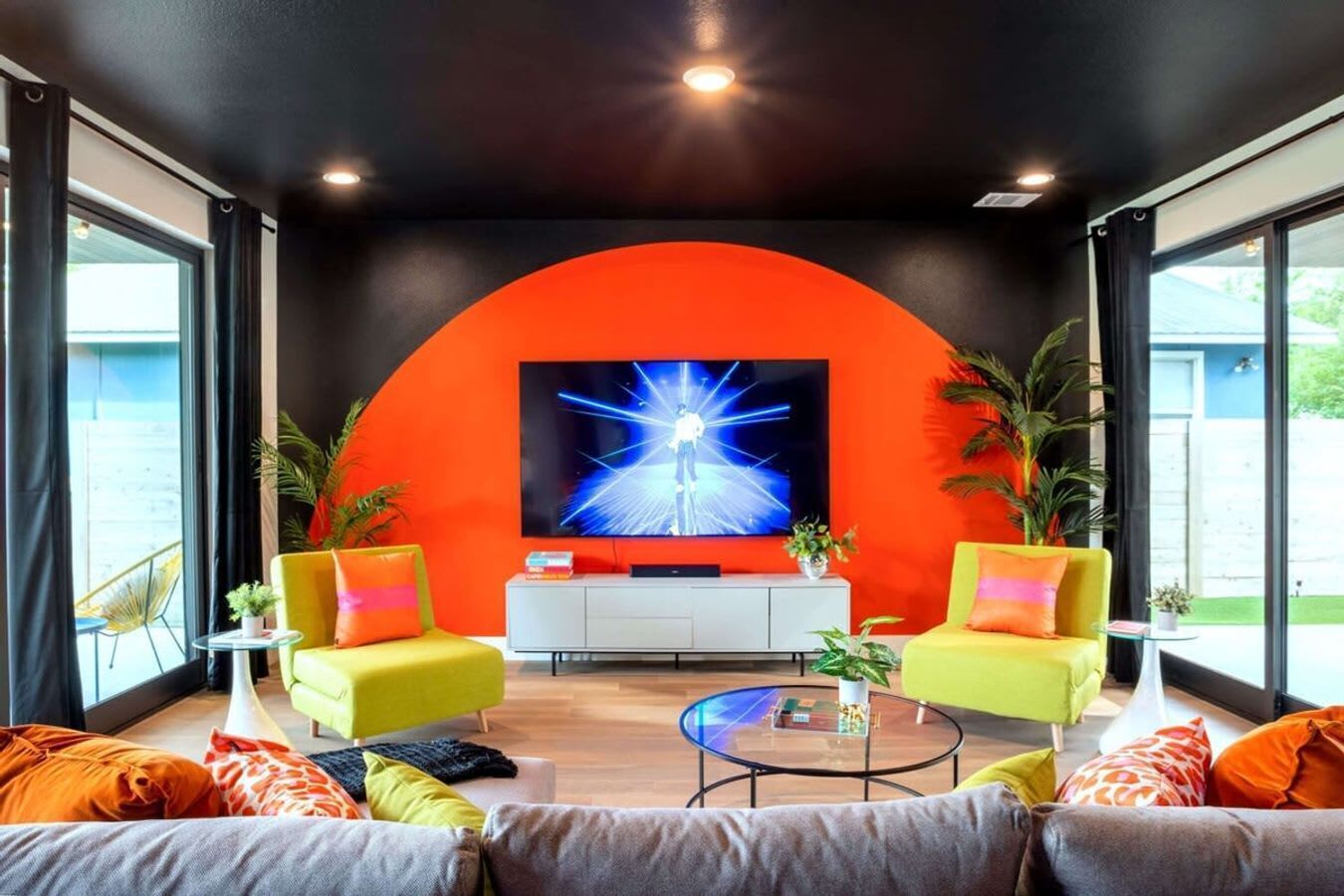 Ein modernes Wohnzimmer mit einem großen Fernseher, einer leuchtend orangefarbenen Akzentwand und bequemen Sitzgelegenheiten.