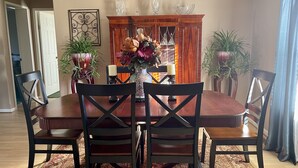 A dining room with a wooden table and four chairs, a floral centerpiece, and a decorative cabinet with glassware. - Mountain View Stay LLC -  The perfect place to get away, relax and enjoy nature. (Mena)