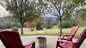A patio area with Adirondack chairs and a fire pit, overlooking a scenic landscape with trees and distant mountains. - Mountain View Stay LLC -  The perfect place to get away, relax and enjoy nature. (Mena)