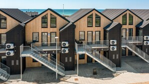 A row of wooden cabins with external air conditioning units, a staircase, and a view of the sea. - Havnehusene, Lejl. 47 (Slagelse)