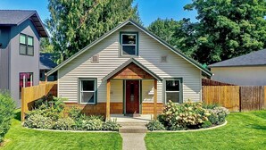 Une maison à deux étages avec un porche à l’avant, une clôture en bois et une pelouse bien entretenue.