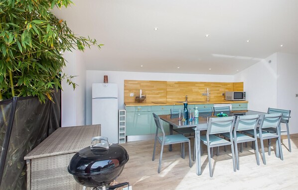 A modern kitchen with a wooden backsplash, a built-in microwave, and a dining area with a table and chairs. - Beach front home in Saint-Laurent-du-Var (Saint-Laurent-du-Var)