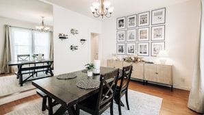 A dining area with a wooden table and chairs, a chandelier, and a wall decorated with framed pictures. - Bright, chic & spacious by Summit/Hamline in St Paul with porch and swing chairs (Saint Paul)