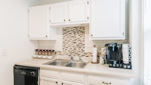 A kitchen with white cabinets, a dishwasher, a coffee maker, and a tiled backsplash. - Bright, chic & spacious by Summit/Hamline in St Paul with porch and swing chairs (Saint Paul)
