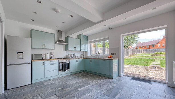 A modern kitchen with light blue cabinets, a built-in oven, and a large window overlooking a garden. - Charming 4 Bedroom Birmingham Home (Birmingham)