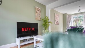 A living room with a flat-screen TV displaying "NETFLIX," a white entertainment unit, a green plant, and artwork on the walls. - Charming 4 Bedroom Birmingham Home (Birmingham)