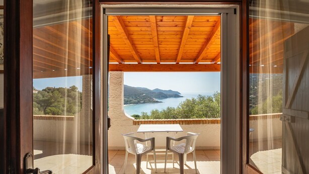 Ein Balkon mit Holzboden und einem Tisch mit zwei Stühlen, mit Blick auf eine schöne Küstenlandschaft.
