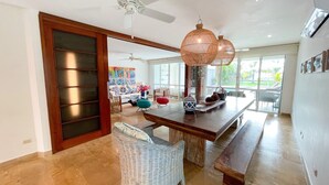 A spacious living area with a wooden dining table, wicker chairs, and a ceiling fan.