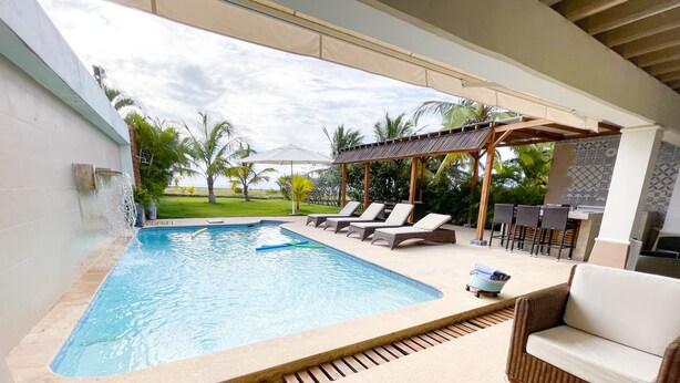 A swimming pool with lounge chairs and a pergola, surrounded by greenery and a view of the sky.