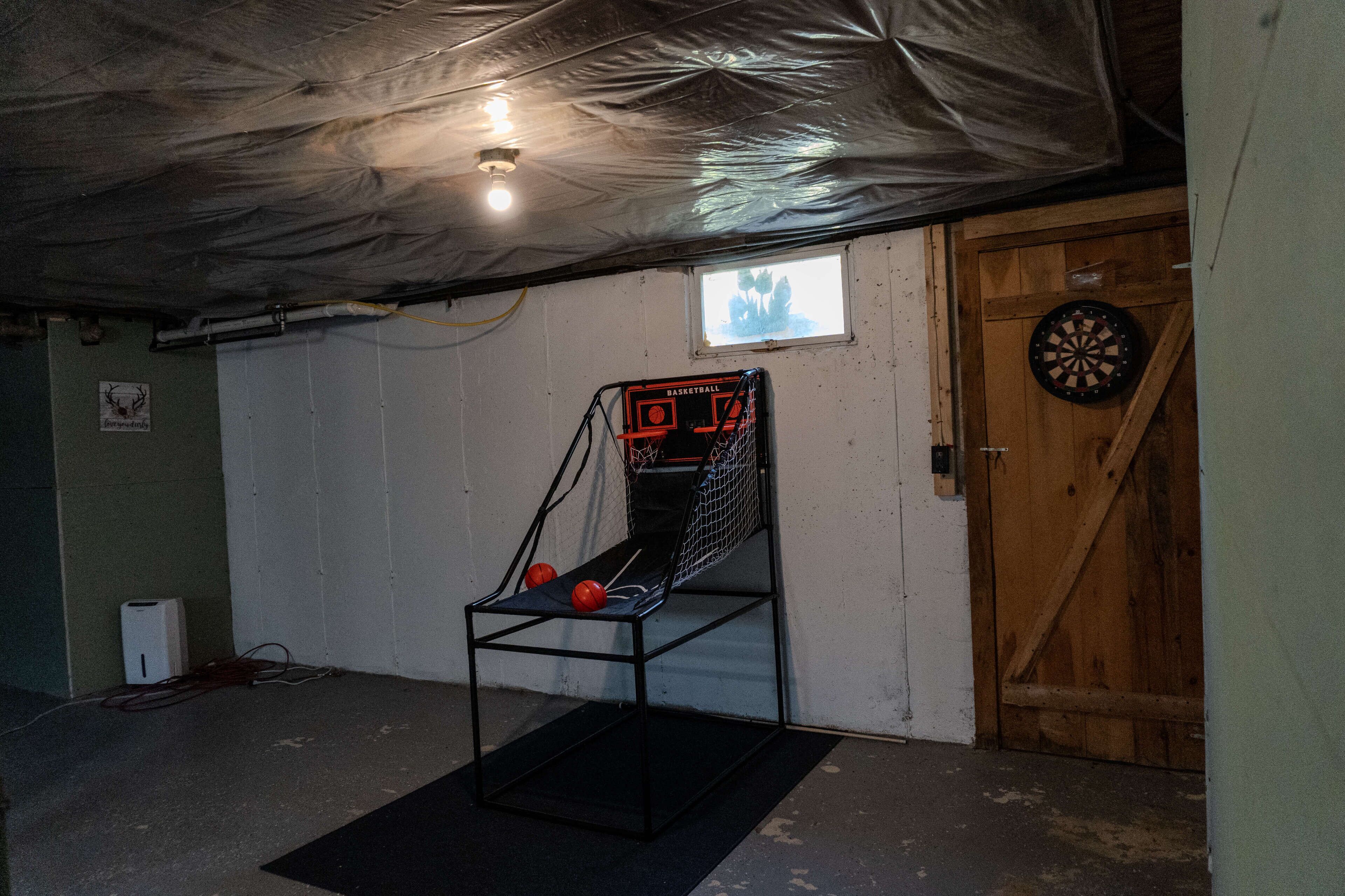 A basement with a basketball arcade, a dartboard, and a wooden door.