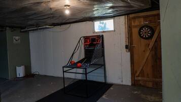 A basement with a basketball arcade, a dartboard, and a wooden door.