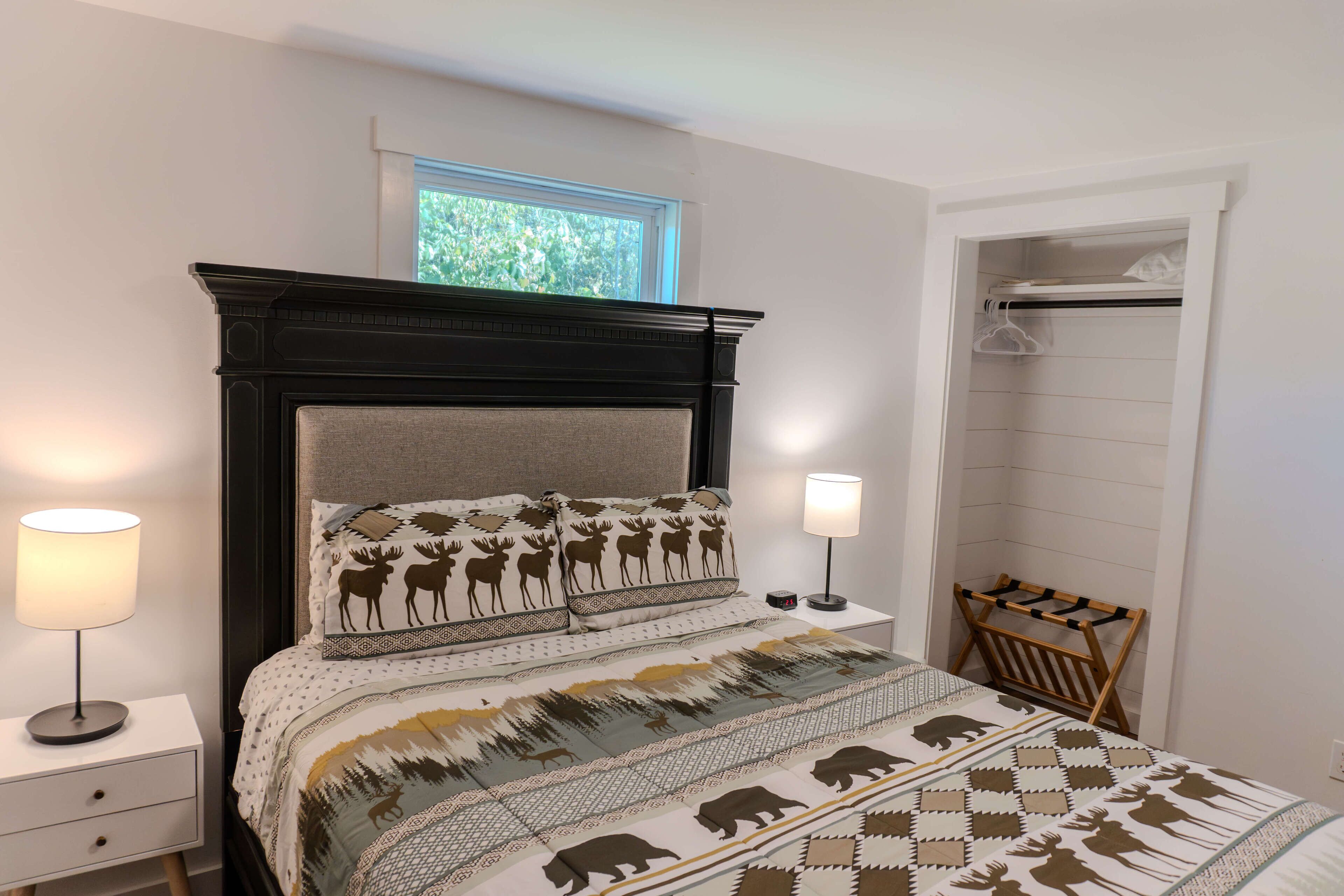 Une chambre à coucher avec un lit agrémenté d’une couvre-lit à motifs, d’une tête de lit en bois, de lampes de chevet, d’une table de chevet et d’une fenêtre donnant sur un paysage verdoyant.