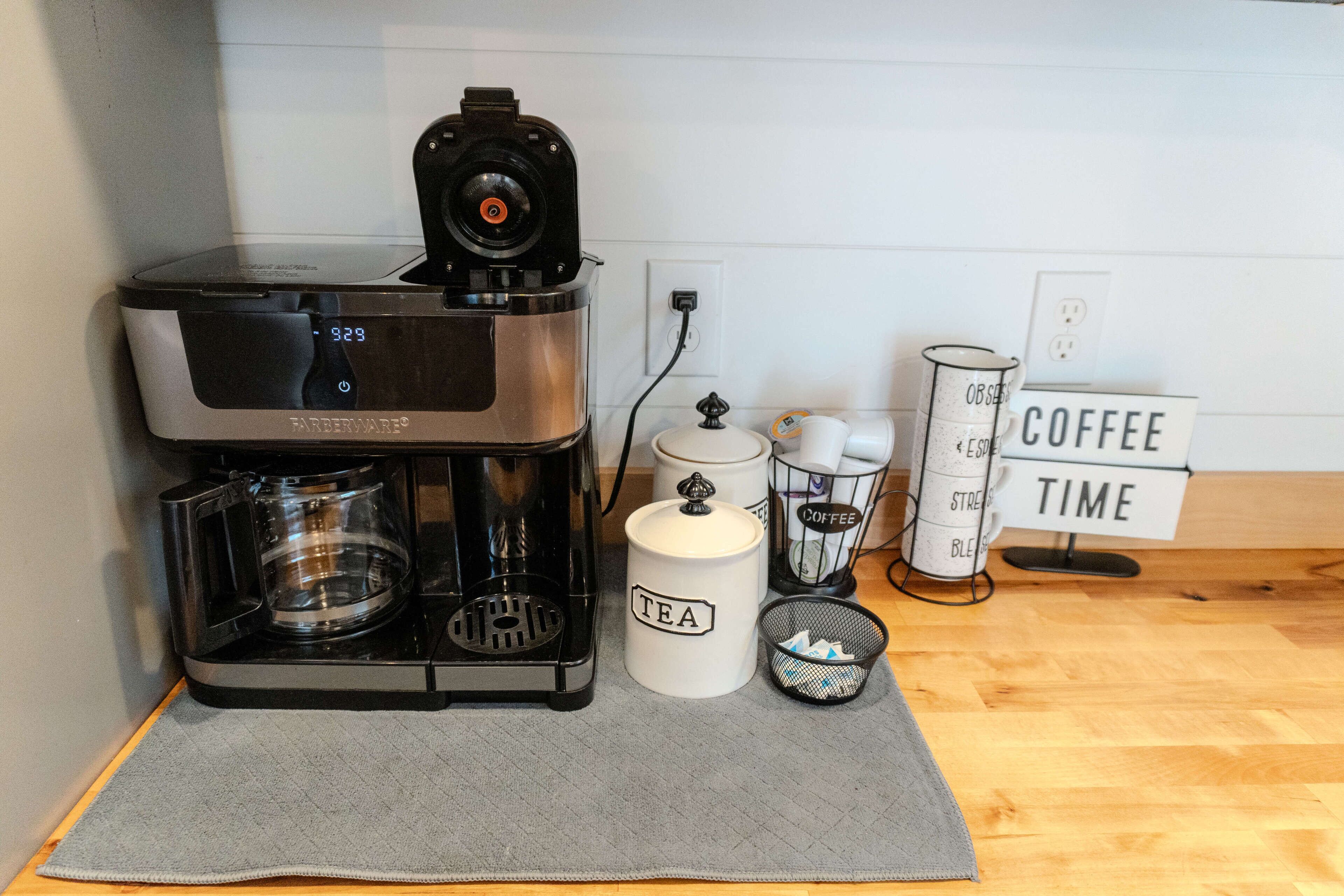 Een koffiezetapparaat, een theecaddy en een bord met koffie-thema op een keukenwerkblad.