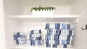 A white closet with shelves holding folded towels and a potted plant. - Deer Ridge A/C, Firepit, Pool Table, Acadia (Ellsworth)
