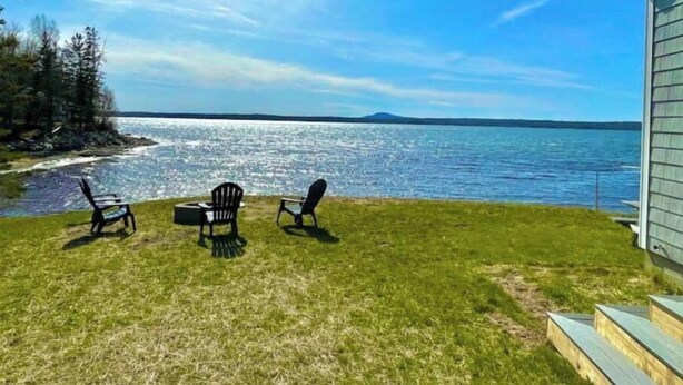 A grassy area with three Adirondack chairs facing a body of water. - Water View home Minutes to all Acadia NP Sites! (Trenton)