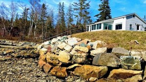 A modern house with a stone wall and a clear view of the surrounding forest. - Water View home Minutes to all Acadia NP Sites! (Trenton)