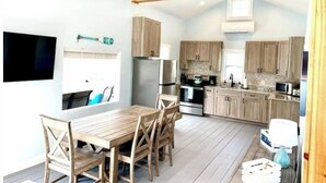 A spacious kitchen with wooden cabinets, a dining table with chairs, a ceiling fan, and a TV mounted on the wall. - Water View home Minutes to all Acadia NP Sites! (Trenton)