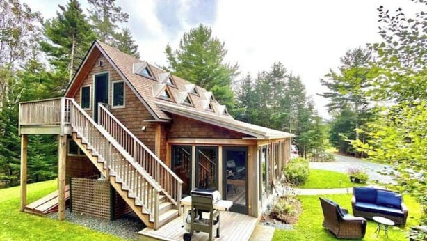 A wooden cabin with a deck, outdoor seating, and a staircase leading to the entrance. - Turnstone Cottage @ Acadia NP (Southwest Harbor)