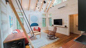 A spacious room with wooden floors, a large TV mounted on the wall, a rocking chair, and a red sofa. - Turnstone Cottage @ Acadia NP (Southwest Harbor)