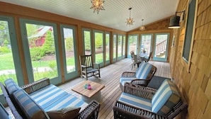A covered outdoor seating area with wicker furniture and striped cushions, large windows, and a wooden deck. - Turnstone Cottage @ Acadia NP (Southwest Harbor)