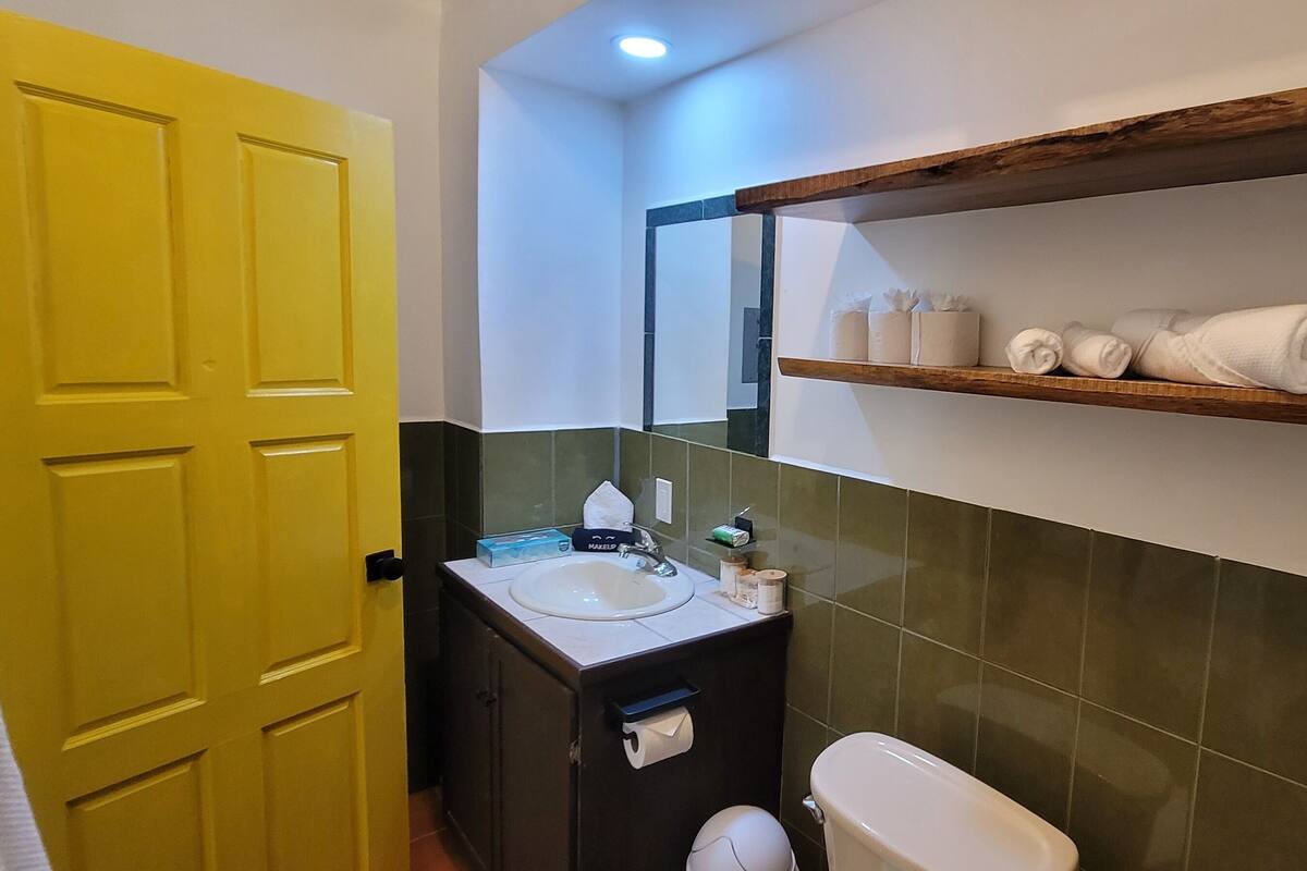 A bathroom with a yellow door, a sink with toiletries, a toilet, and a shelf with towels.