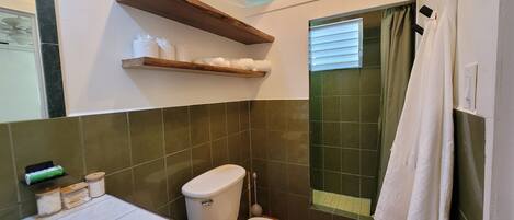 A bathroom with green tiles, a toilet, a shelf with toiletries, and a shower curtain.