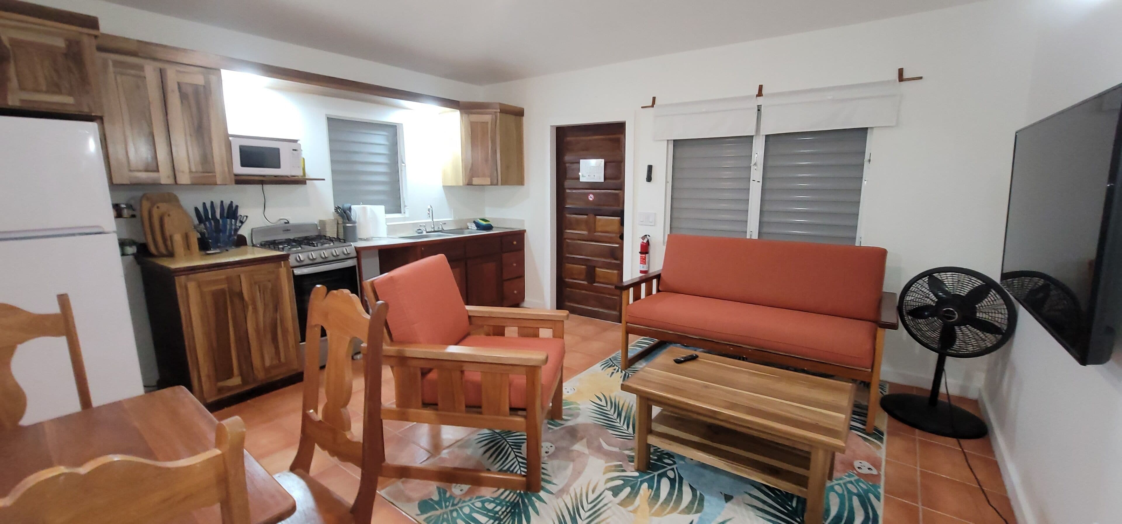 A compact living space with a kitchenette, wooden furniture, a sofa, and a fan.