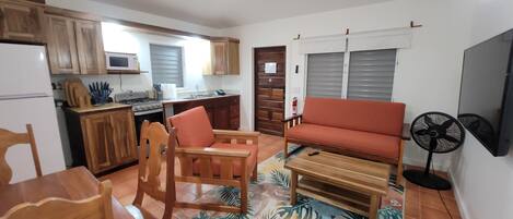 A compact living space with a kitchenette, wooden furniture, a sofa, and a fan.