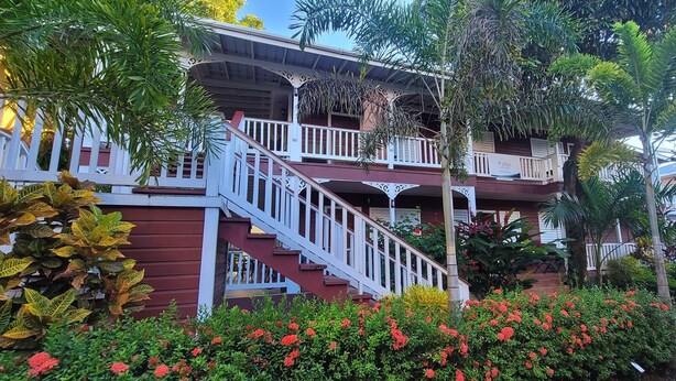 Un edificio de varios pisos con una escalera destacada, rodeado de abundante vegetación y plantas con flores.