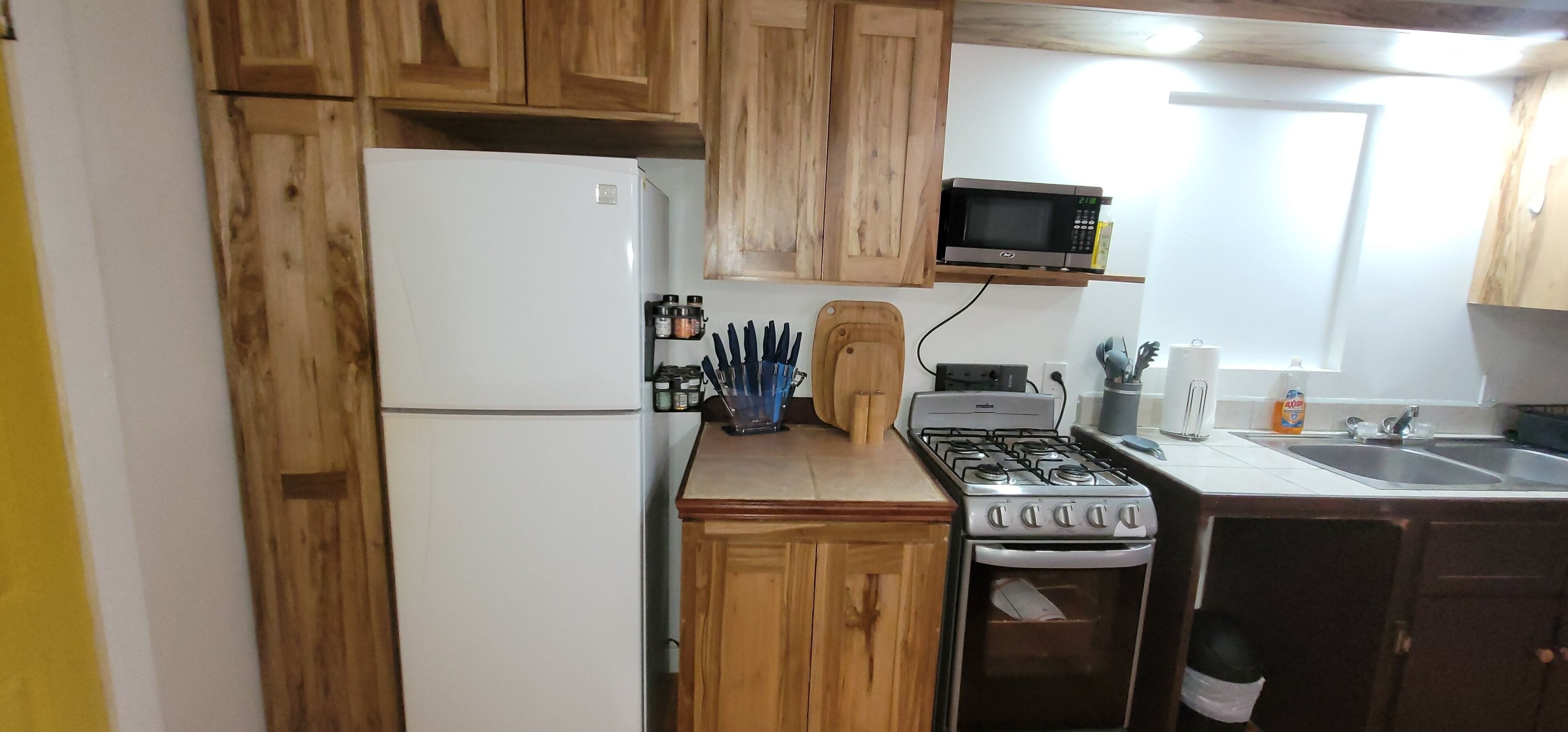 A compact kitchen with wooden cabinets, a white refrigerator, a microwave, a gas stove, and a sink.