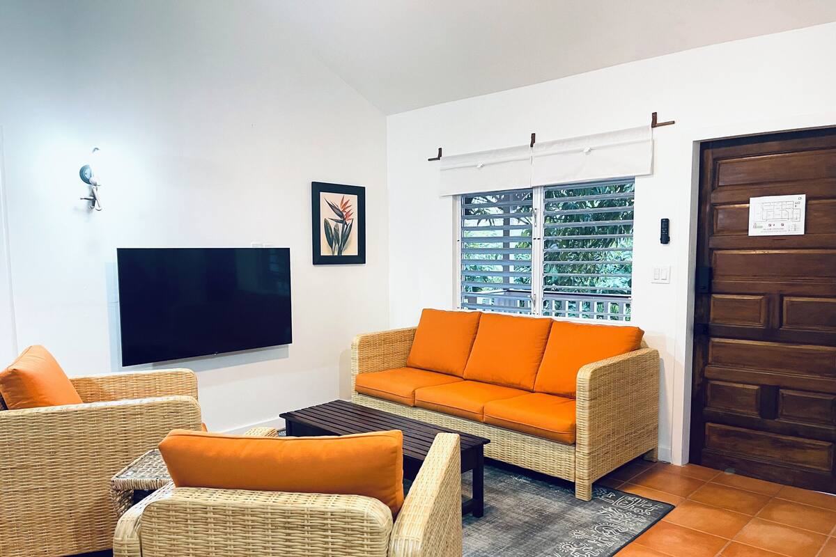 A living room with wicker furniture, a flat-screen TV, and a window with blinds.