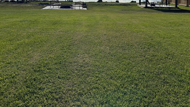 A grassy area with a wooden deck and a gazebo overlooking a lake with mountains in the background.
