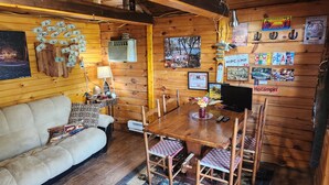 A cozy cabin interior with a wooden dining table, chairs, a sofa, and a TV.