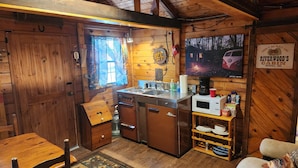 A cabin interior with wooden walls, a kitchen area including a stove, sink, and microwave, and a dining area with a table and chairs.