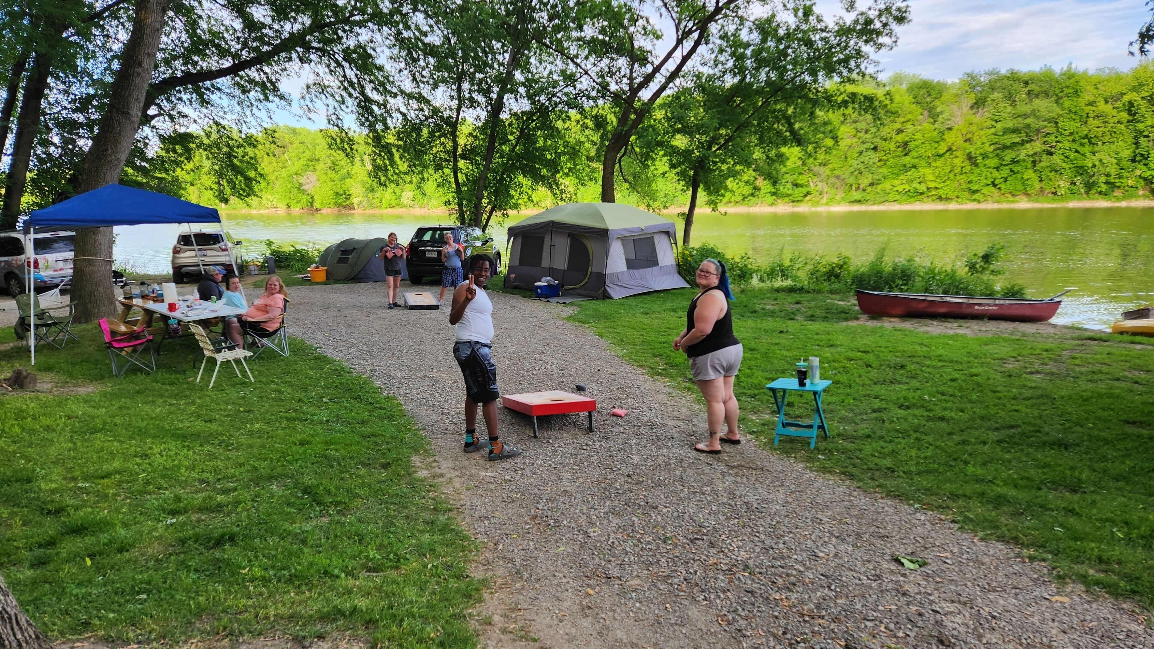 Um camping com tendas, uma mesa e um barco à beira de um lago.