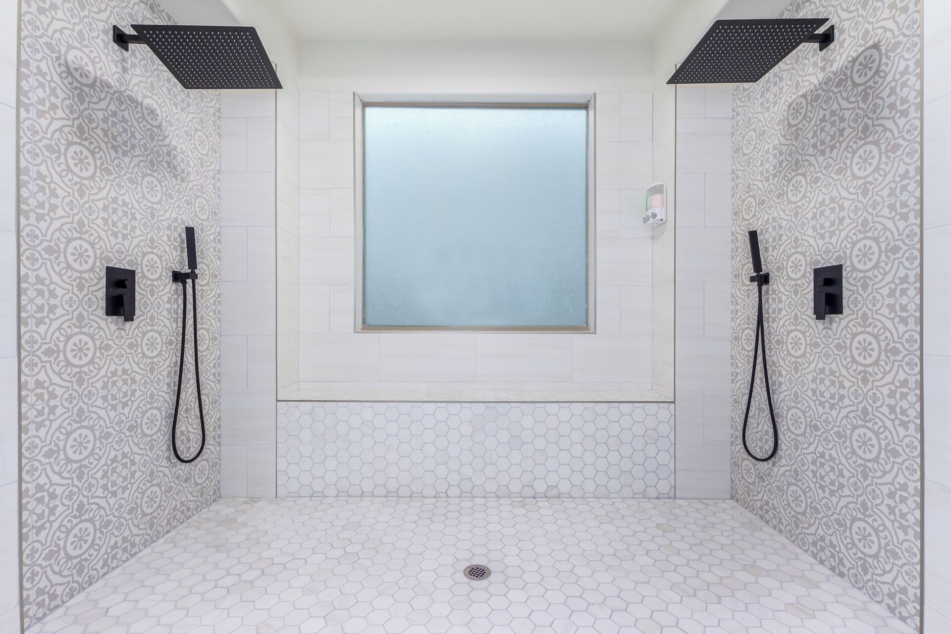 Une salle de bain dotée d’une grande fenêtre, de deux pommes de douche et de murs à motifs.