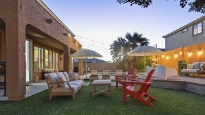 An outdoor patio with a brick wall, string lights, and outdoor furniture including a red chair and a white table. - NEW! Sleeps 24+ House w/Heated Pool, Arcades, Soda Fountain (Mesa)