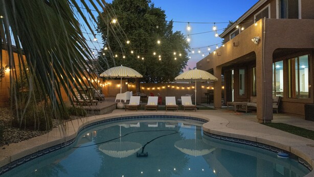 A swimming pool with lounge chairs and umbrellas, surrounded by string lights and palm trees. - NEW! Sleeps 24+ House w/Heated Pool, Arcades, Soda Fountain (Mesa)
