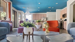 A modern living room with a blue ceiling, a kitchen with pink cabinets, and a dining area with a white table and purple chairs. - NEW! Sleeps 24+ House w/Heated Pool, Arcades, Soda Fountain (Mesa)