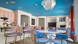 A modern kitchen with pink cabinets, a central island with bar stools, and a dining area with a round table and blue chairs. - NEW! Sleeps 24+ House w/Heated Pool, Arcades, Soda Fountain (Mesa)
