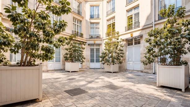 Un cortile con pavimentazione in pietra, piante in vaso e un edificio con numerosi balconi.