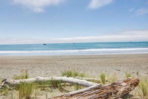 Une plage avec un tronc d’arbre au premier plan, une mer calme et des bateaux au loin.