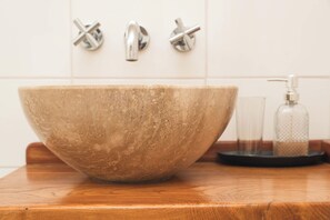 A large, rustic stone basin on a wooden countertop with a modern faucet and soap dispenser in the background. - BORIES - Boutique Guest House (Natales)