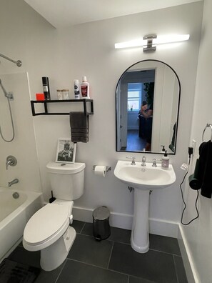 Bathroom features a pedestal sink, bathtub, and toilet, with a shelf for toiletries and a framed photo.