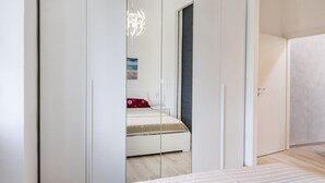 A bedroom with a bed, a wardrobe, and a mirror reflecting a bed and a painting. - S311 - Sirolo, new two-room apartment completely renovated (Sirolo)
