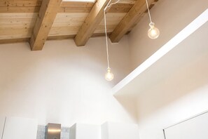 A room with exposed wooden beams, a white ceiling, and two hanging light fixtures.