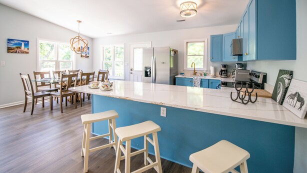 A modern kitchen with a large island, blue cabinets, and a dining area with wooden chairs and a glass table.