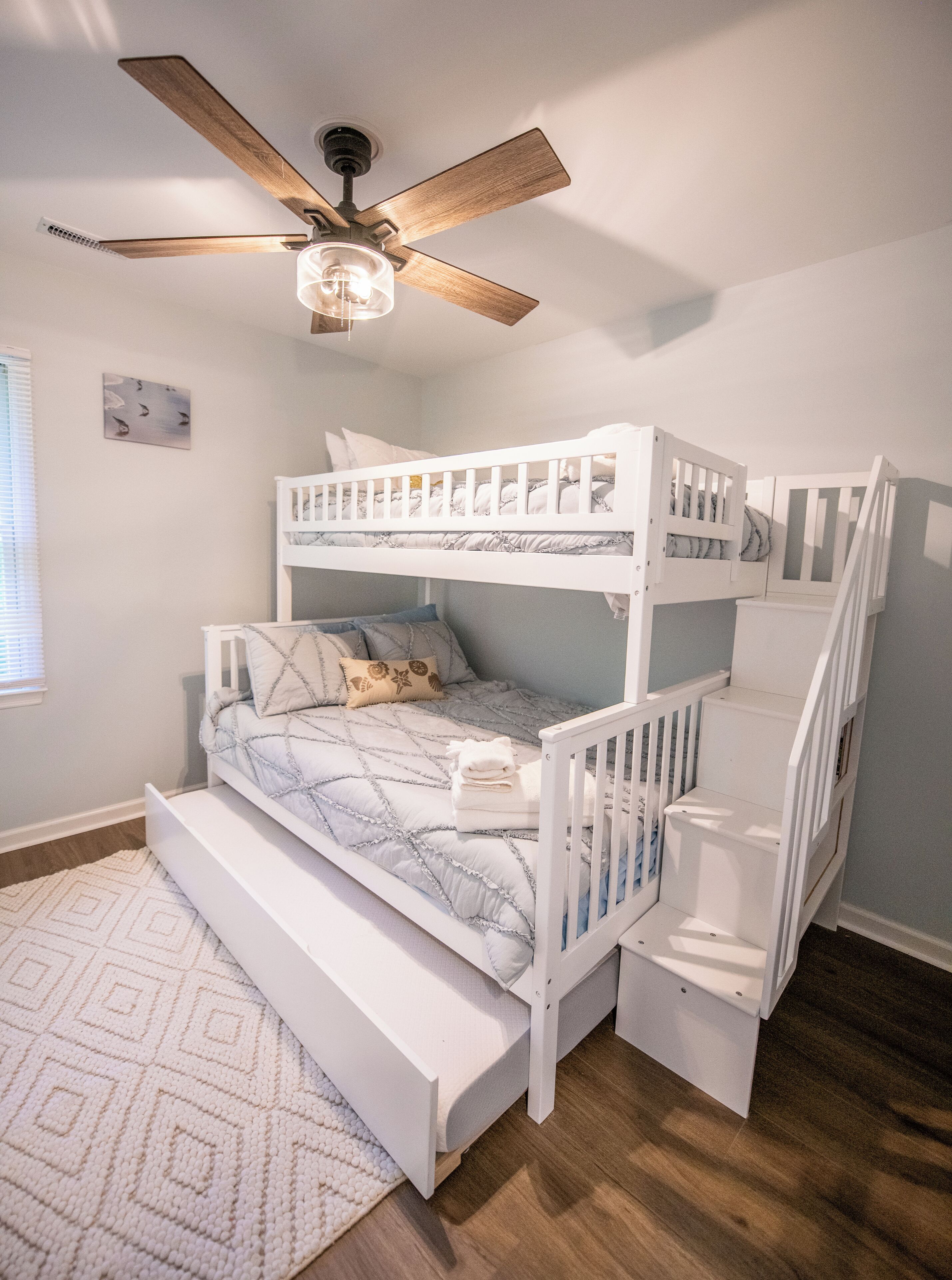 A bunk bed room with a ceiling fan, a white wall, and a patterned rug.
