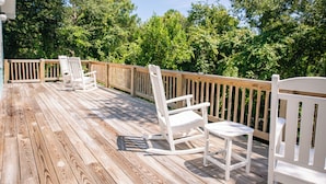 A wooden deck with white rocking chairs and a wooden railing.
