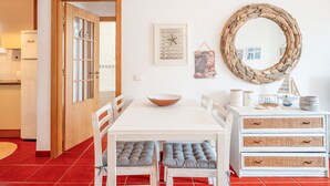Un área de comedor con una mesa blanca, sillas grises con acolchado, una puerta de madera, un mapa, un espejo y un aparador con adornos.